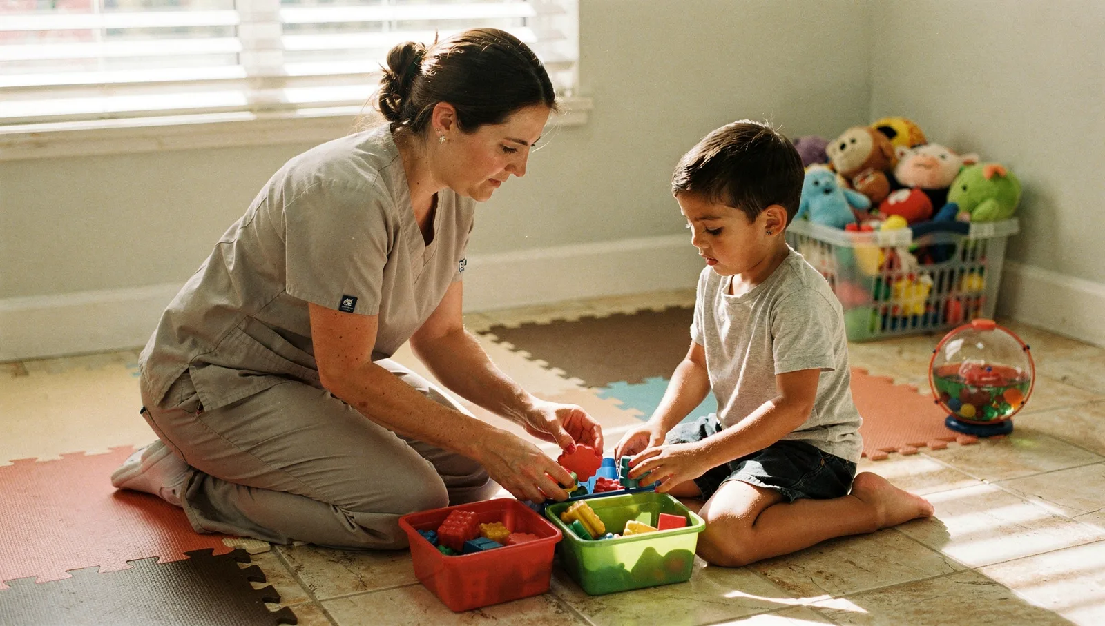 A behavior technician kneels beside a child, guiding their hand to sort colored plastic shapes into matching bins.
