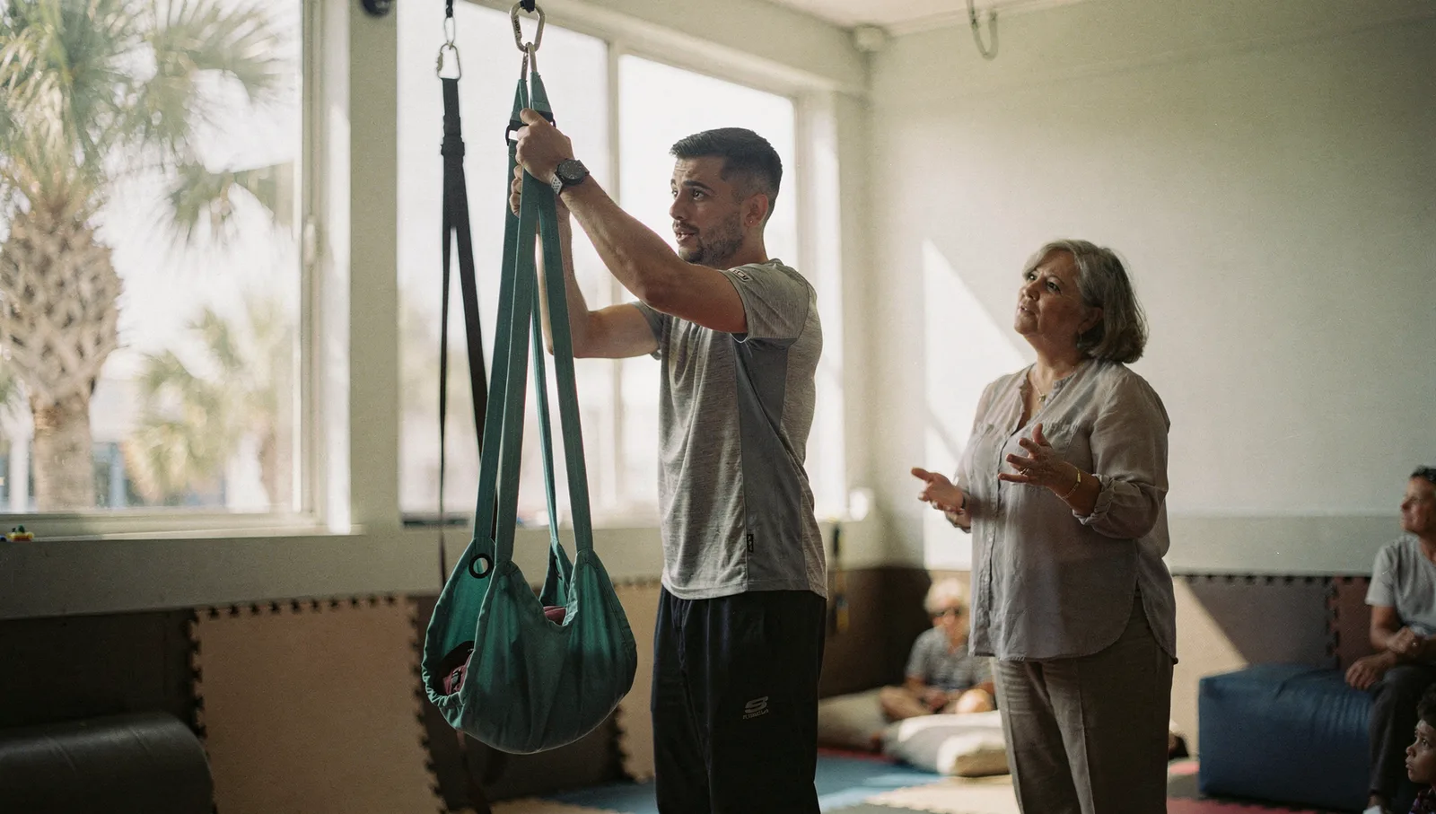 A behavior technician adjusts a pediatric therapy swing as a supervisor observes in a sensory gym.